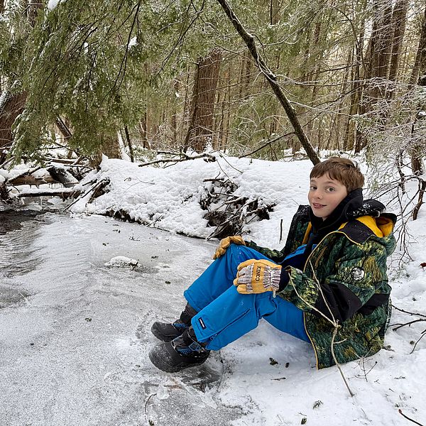 Smiling child at the edge of a frozen stream in winter.